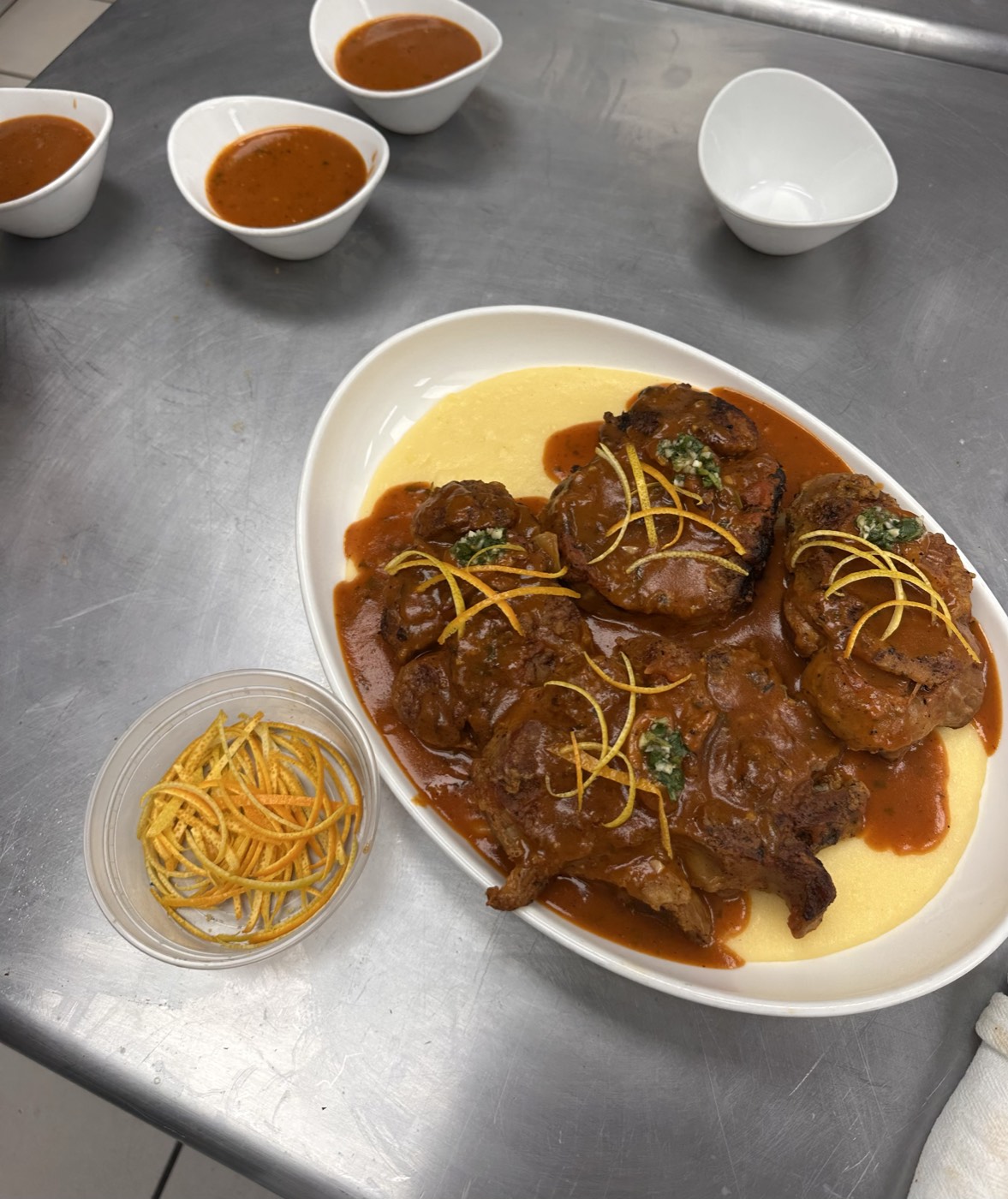 Braised veal shanks in tomato sauce plated over polenta, finished with gremolata and strands of citrus zest